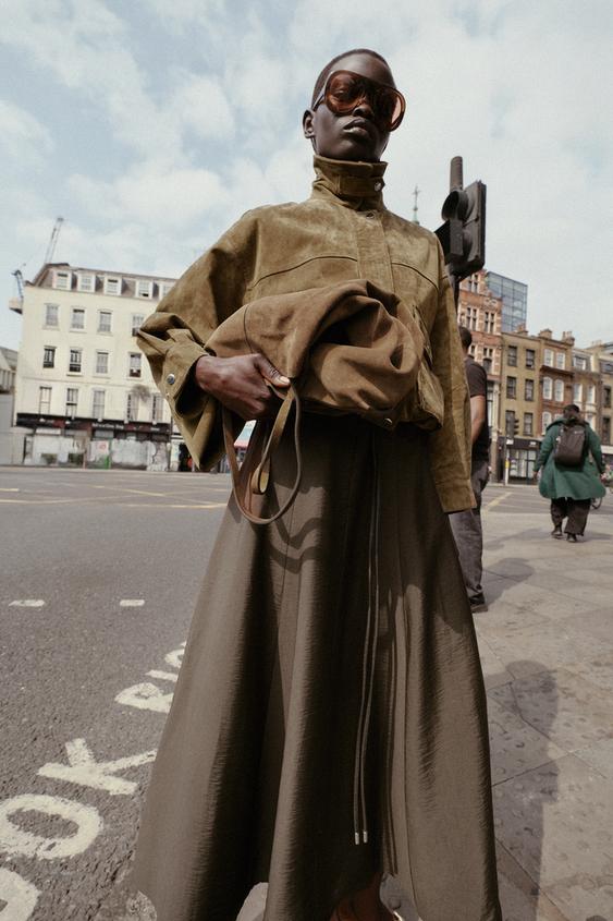 Souprava khaki bomber bundy s košilovým límcem a dlouhými rukávy, khaki široké sukně a ladící kabelky.
