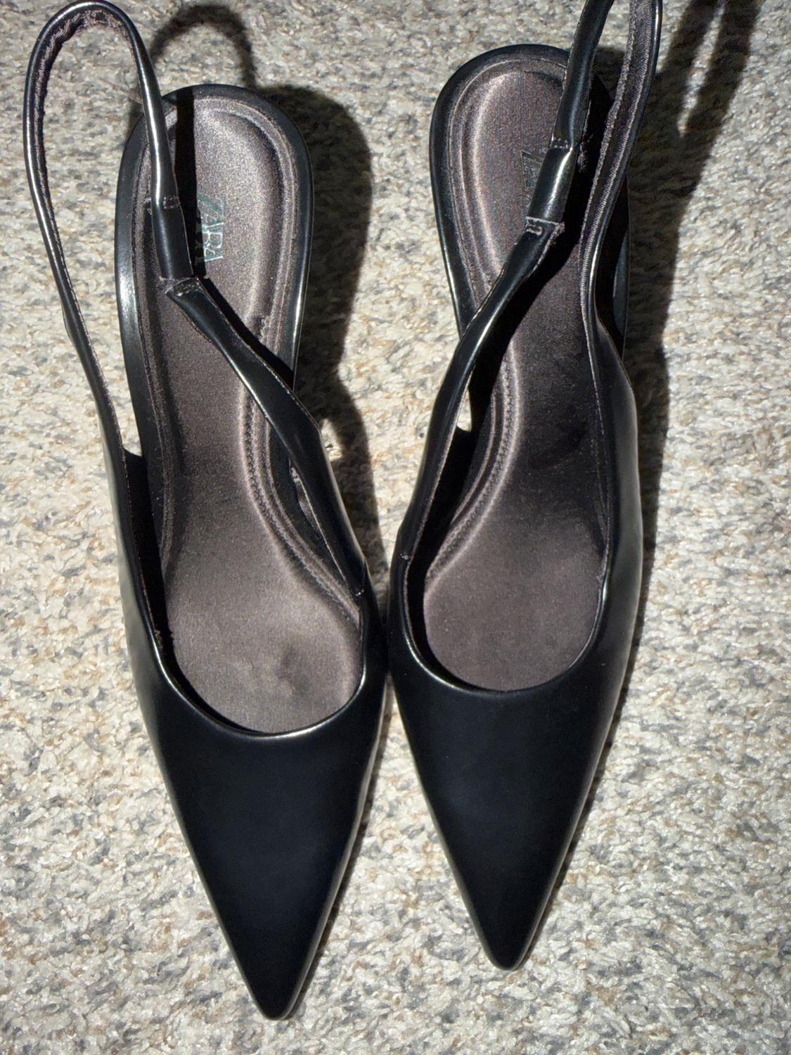 Black pointed-toe high heels with thin straps, on a gray carpet.