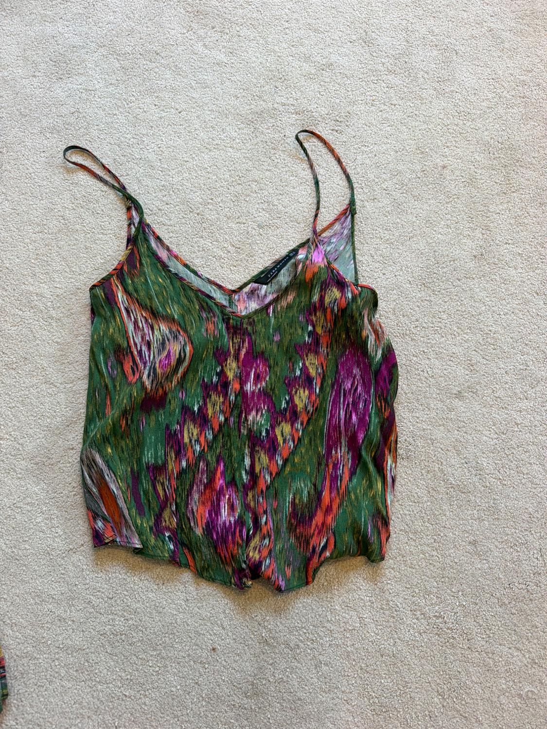 Cami top with an abstract print in shades of green, purple and orange, on a beige rug.