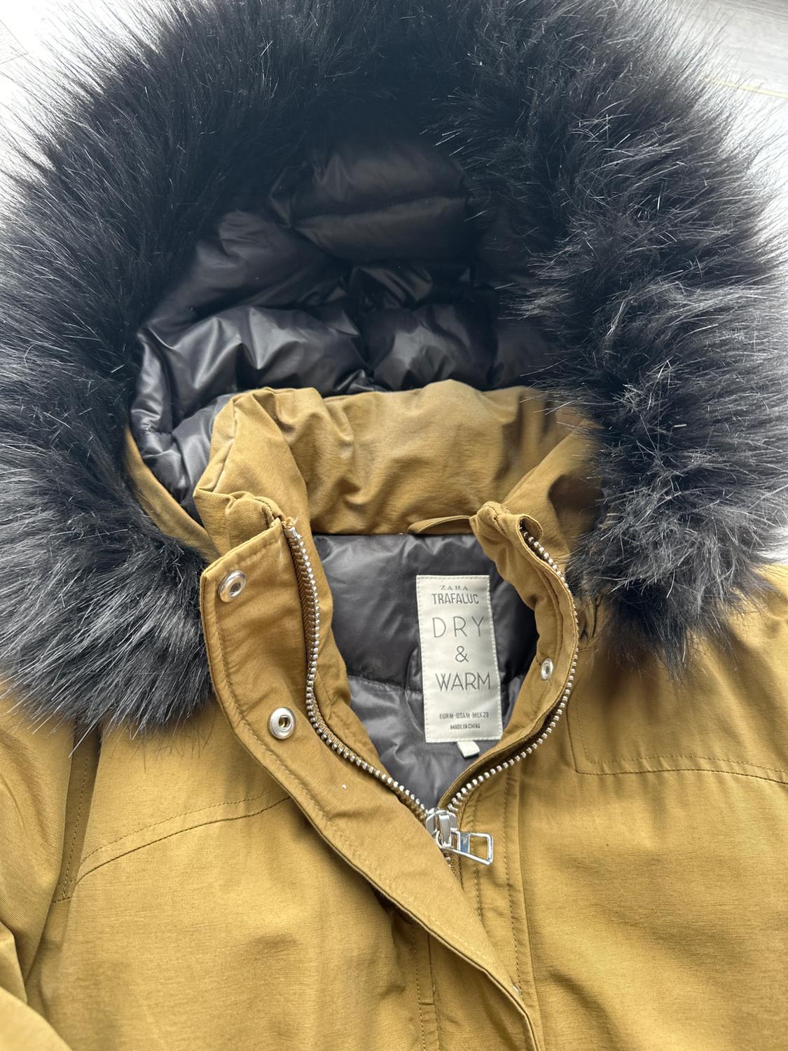 Brown jacket with a black faux-fur trimmed hood and visible label that reads "ZARA TRAFALUC DRY & WARM". Metal zip fastening.