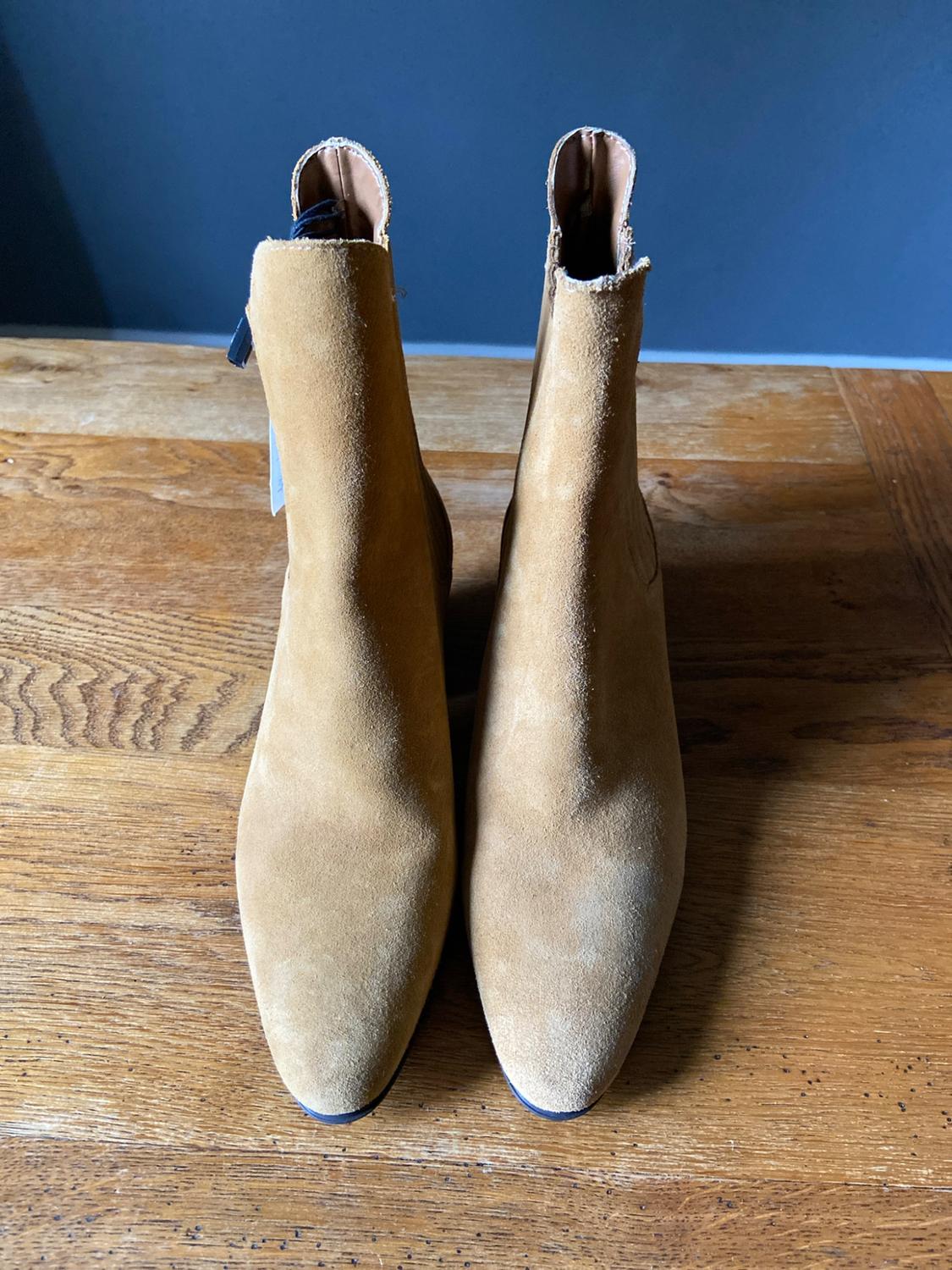Pair of camel suede ankle boots on a wooden table with a dark blue background.
