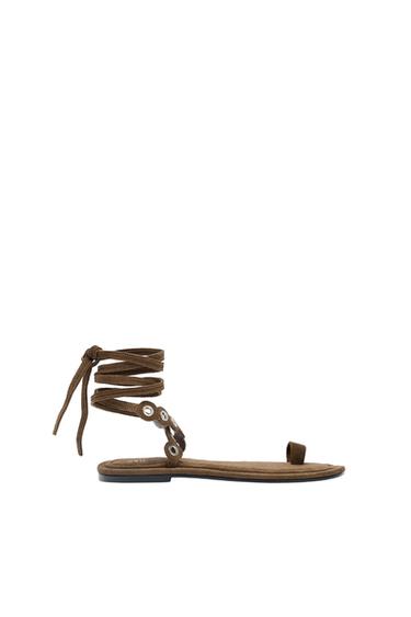 Brown sandal with adjustable straps and metallic details, side view on white background.