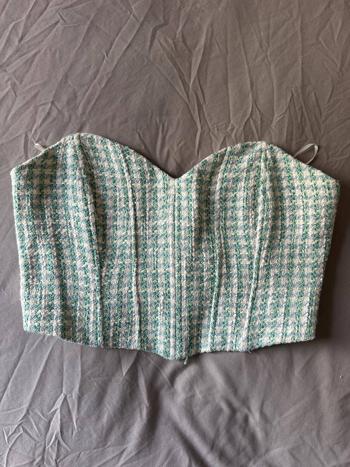 Strapless corset top with a sweetheart neckline and seams. Textured fabric in white, green, and blue, over a crinkled grey fabric background.