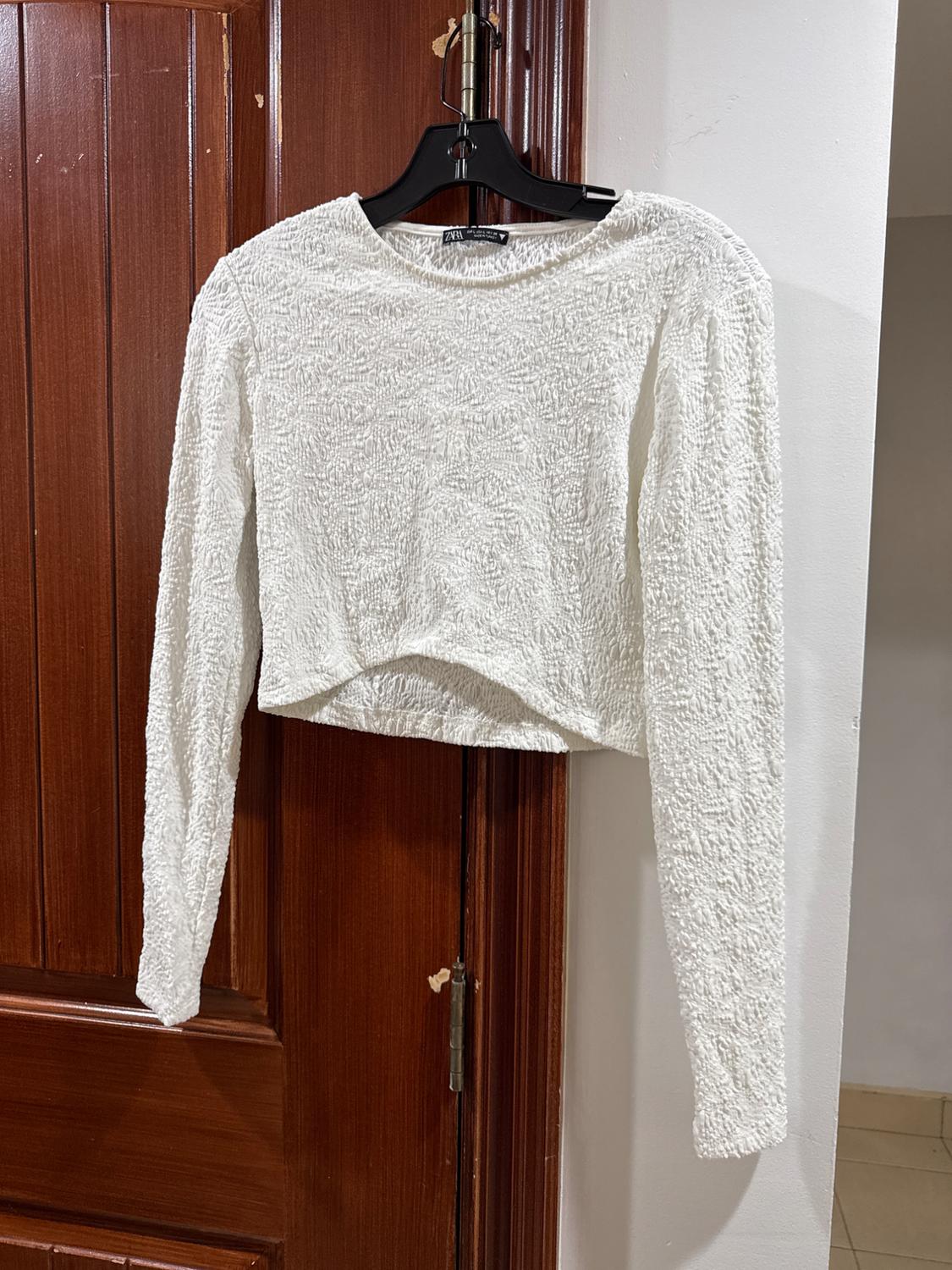 Textured, long-sleeved white sweater hanging on a black hanger over a brown wooden door.