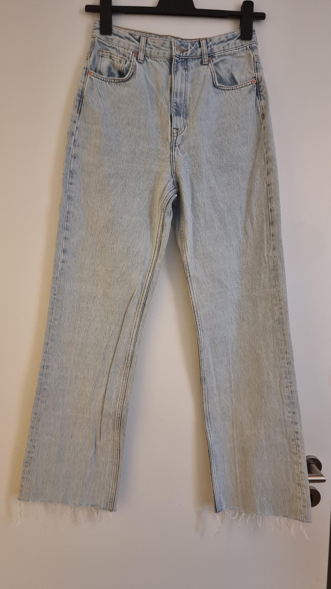 Light blue denim jeans with a frayed hem, hanging on a black hanger against a white background.