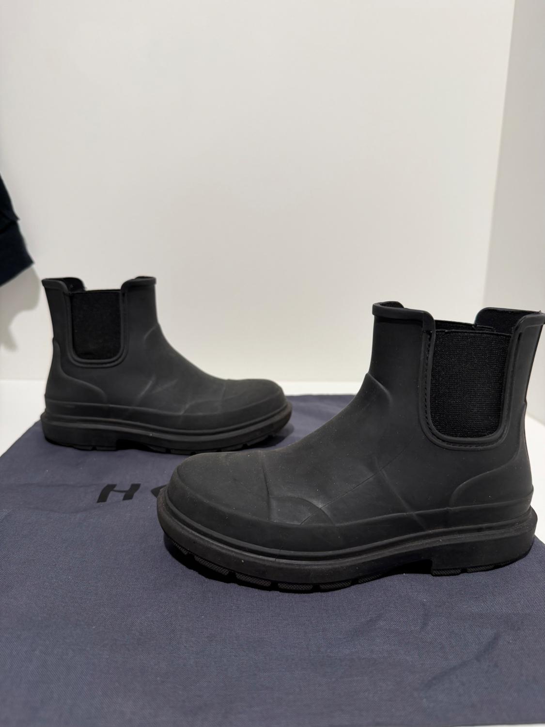 Two black waterproof ankle boots with elasticated side panels on a dark fabric featuring a visible H, against a white background.