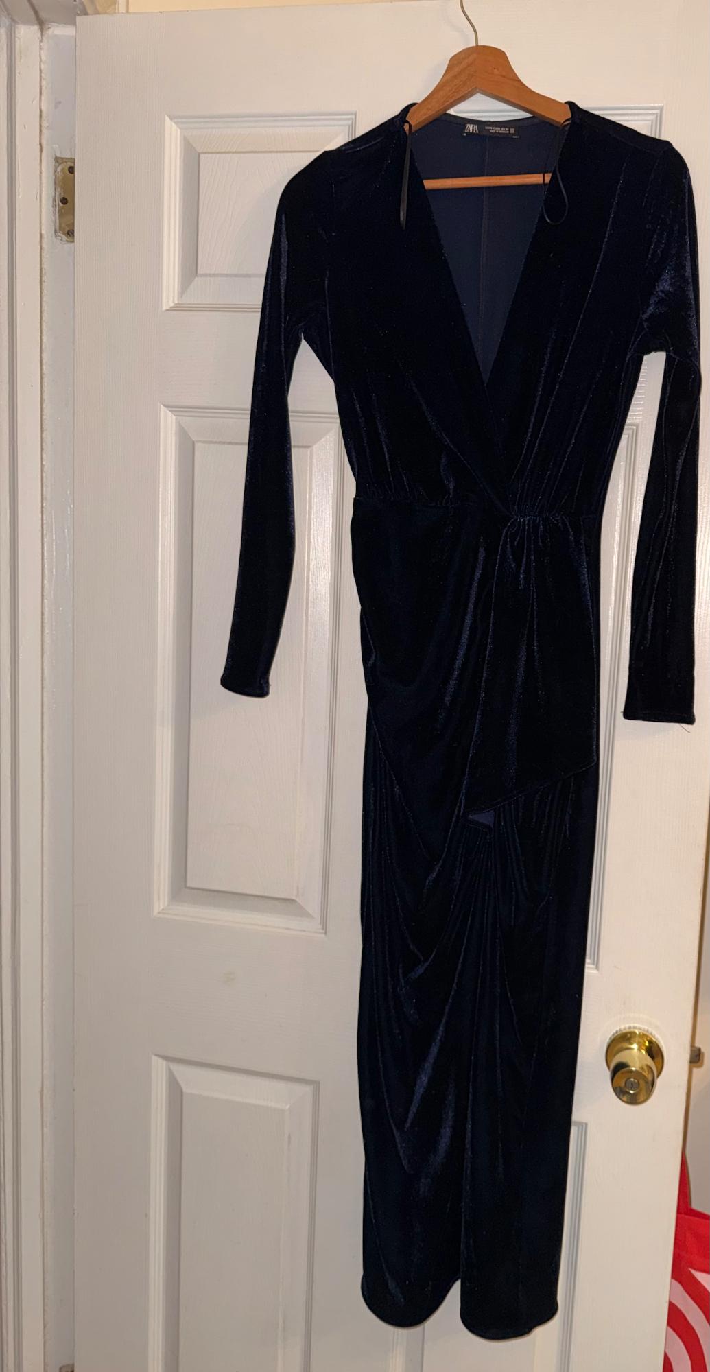 Black velvet dress with long sleeves hanging on a white door.