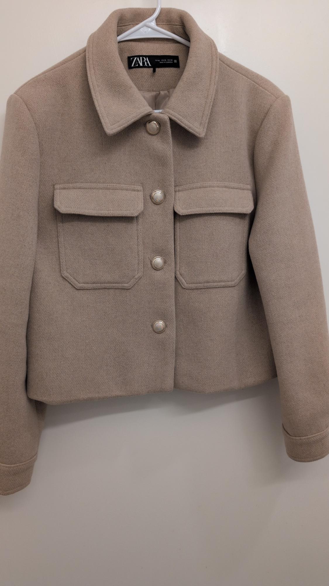 Beige wool jacket with silver buttons and front pockets, hanging on a white hanger. Visible label: ZARA.
