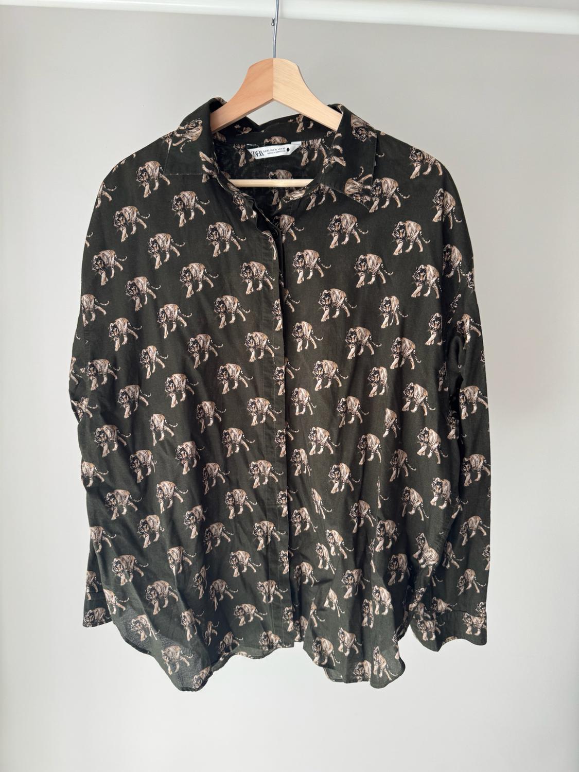 Dark green long-sleeved shirt with a tiger print, hanging on a wooden hanger against a white background.