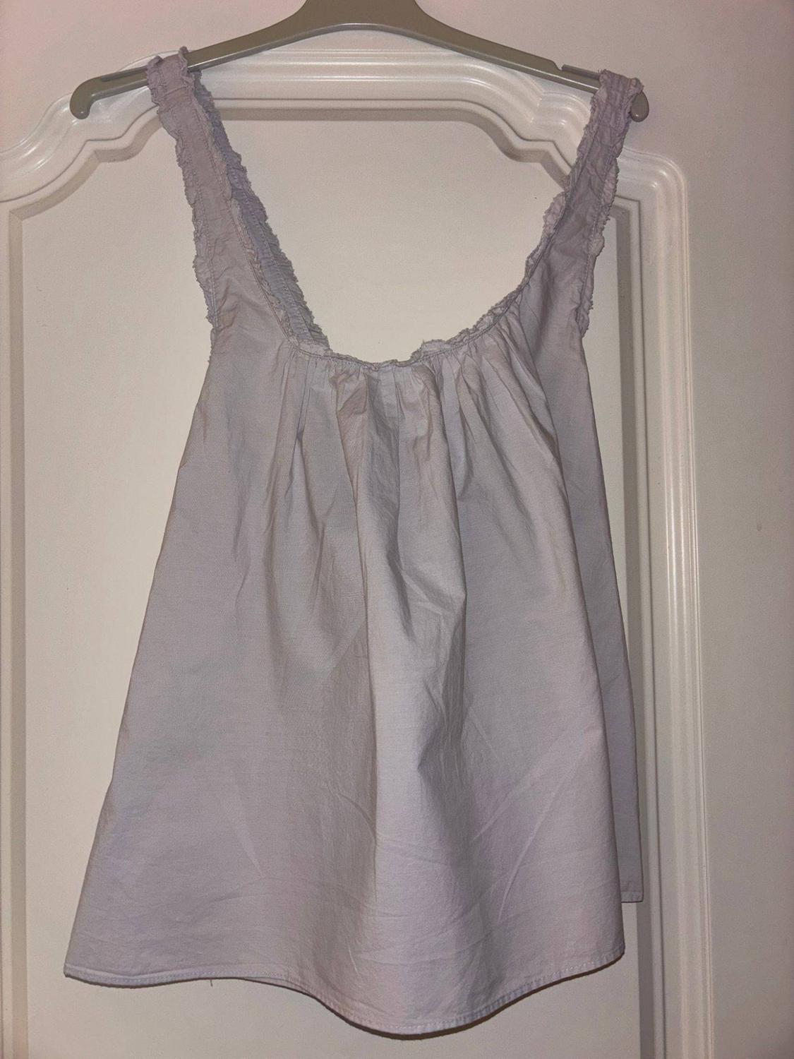 Clear, fluid top with wide shoulder straps and ruched details, hanging on a coat hanger over a white door.
