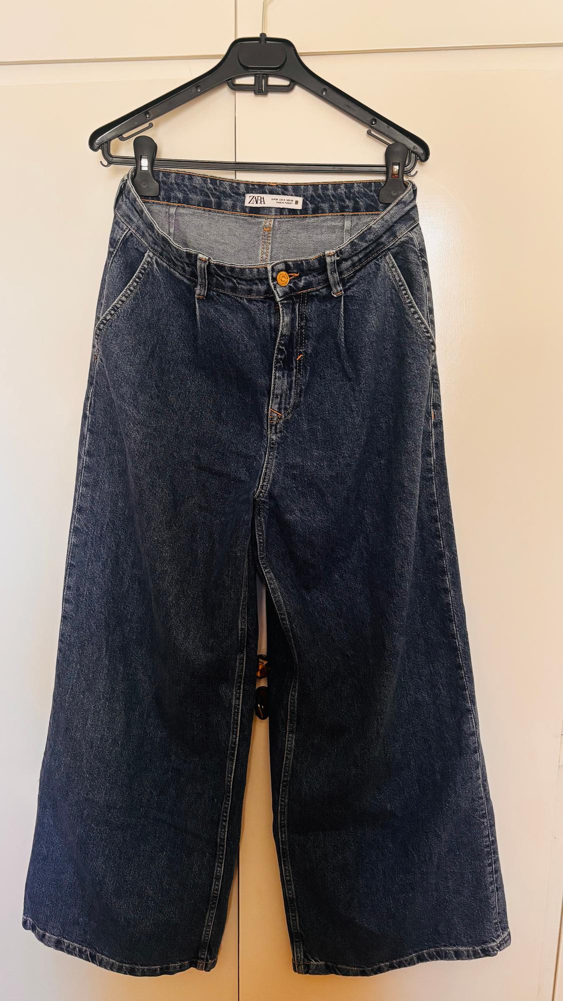 Dark blue denim wide-leg jeans hanging on a black hanger, with a visible ZYA brand label.