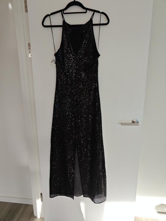 Black sequined dress hanging on a black hanger over a white door, illuminated by natural light.