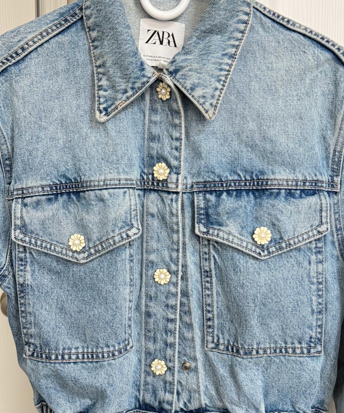Light blue denim jacket with flower-shaped buttons and chest pockets. Visible interior label with the text ZARA.