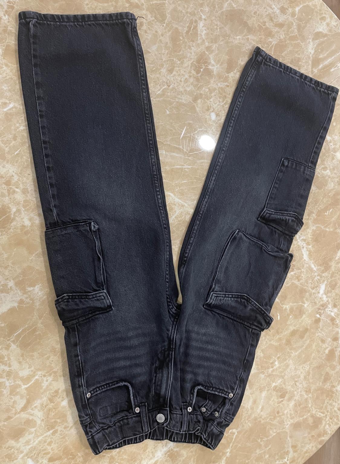 Washed black cargo jeans with an elasticated waist and pockets, laid out in a V-shape on a beige marble surface.