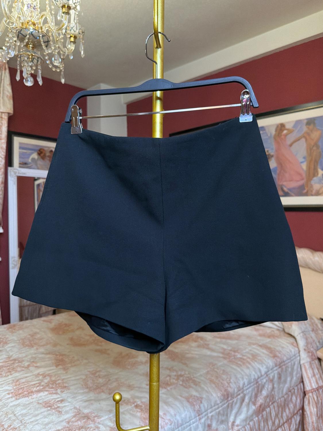 Black shorts hanging on a gold clothes rail in a room with red walls and a chandelier.