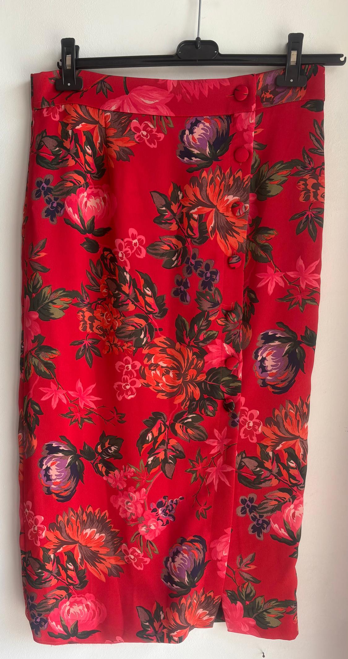 Red skirt with a floral print in orange, pink, and green tones, hanging on a black hanger against a white background.
