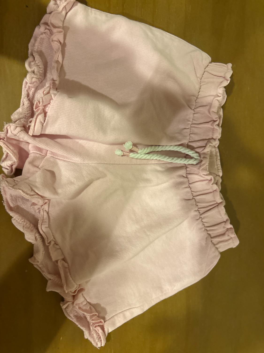 Pink shorts with frills on the edges and a white drawstring at the waist, on a light wooden surface.