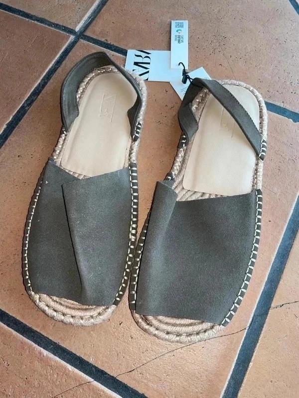 Brown sandals with an espadrille sole on a tiled floor. Visible label with text "ZARA".