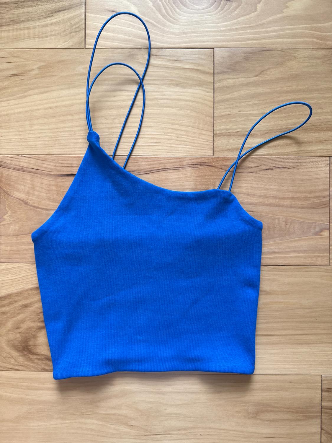 Shiny blue tank top with spaghetti straps on a light wood background with visible grain.