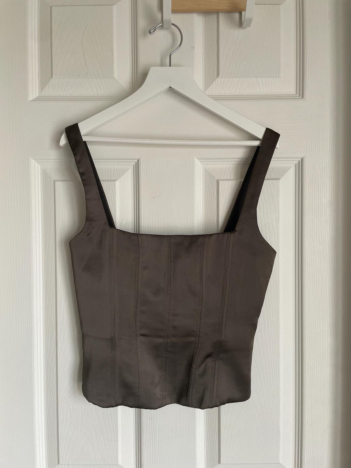 Dark brown wide-strap top hanging on a white hanger over a white panelled door.