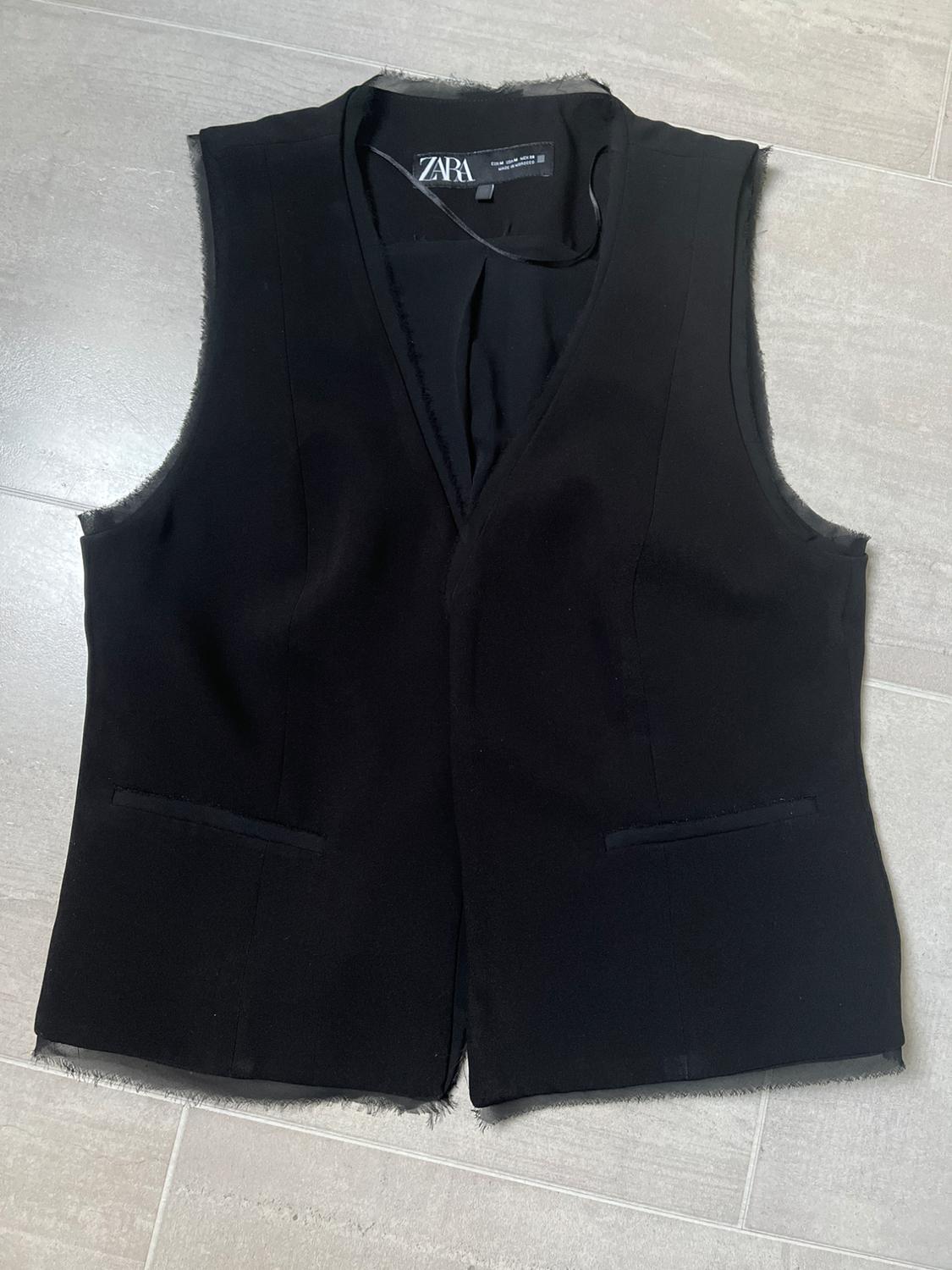 Black sleeveless Zara waistcoat on a grey floor, with frayed edges and a visible label inside the collar.