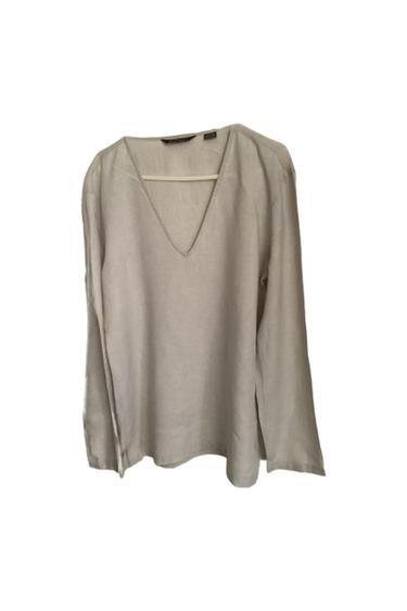 Beige long-sleeved V-neck shirt hanging on a hanger against a white background. Minimalist and relaxed style.