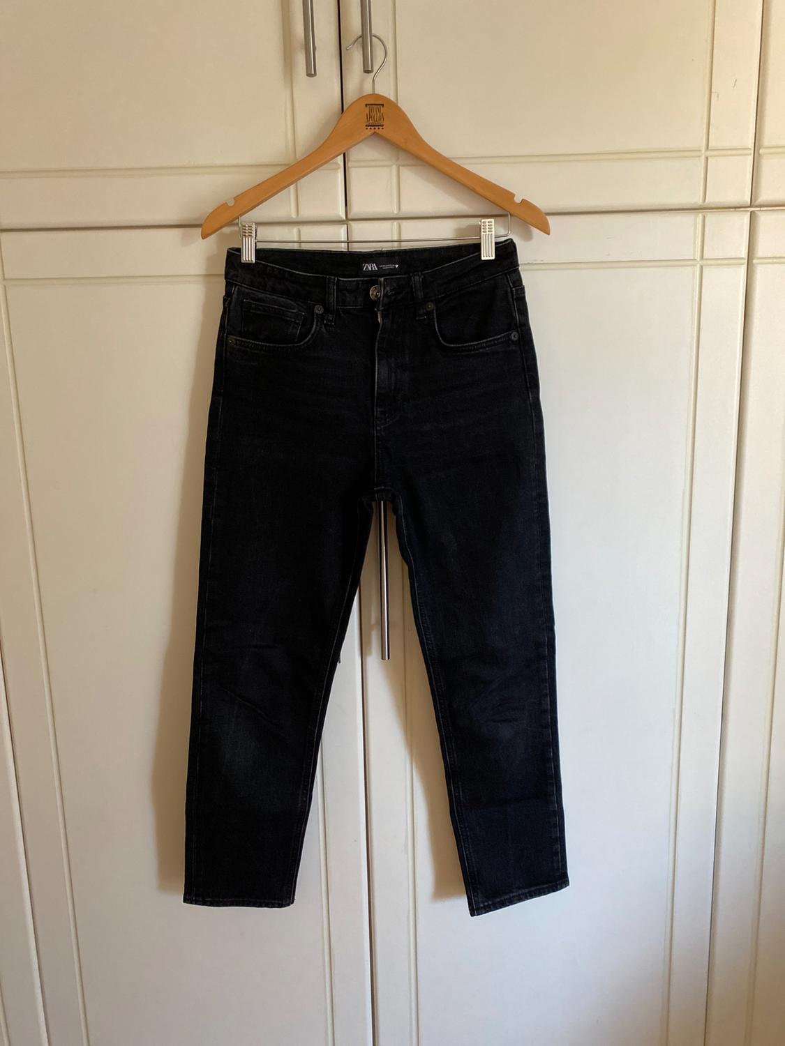 Black jeans hanging on a wooden hanger in front of a white wardrobe.