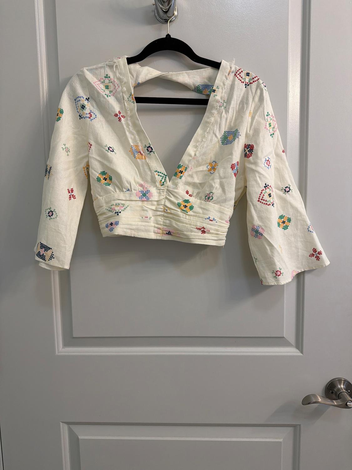 White blouse with a colorful floral and geometric print, hanging on a black hanger over a white door.