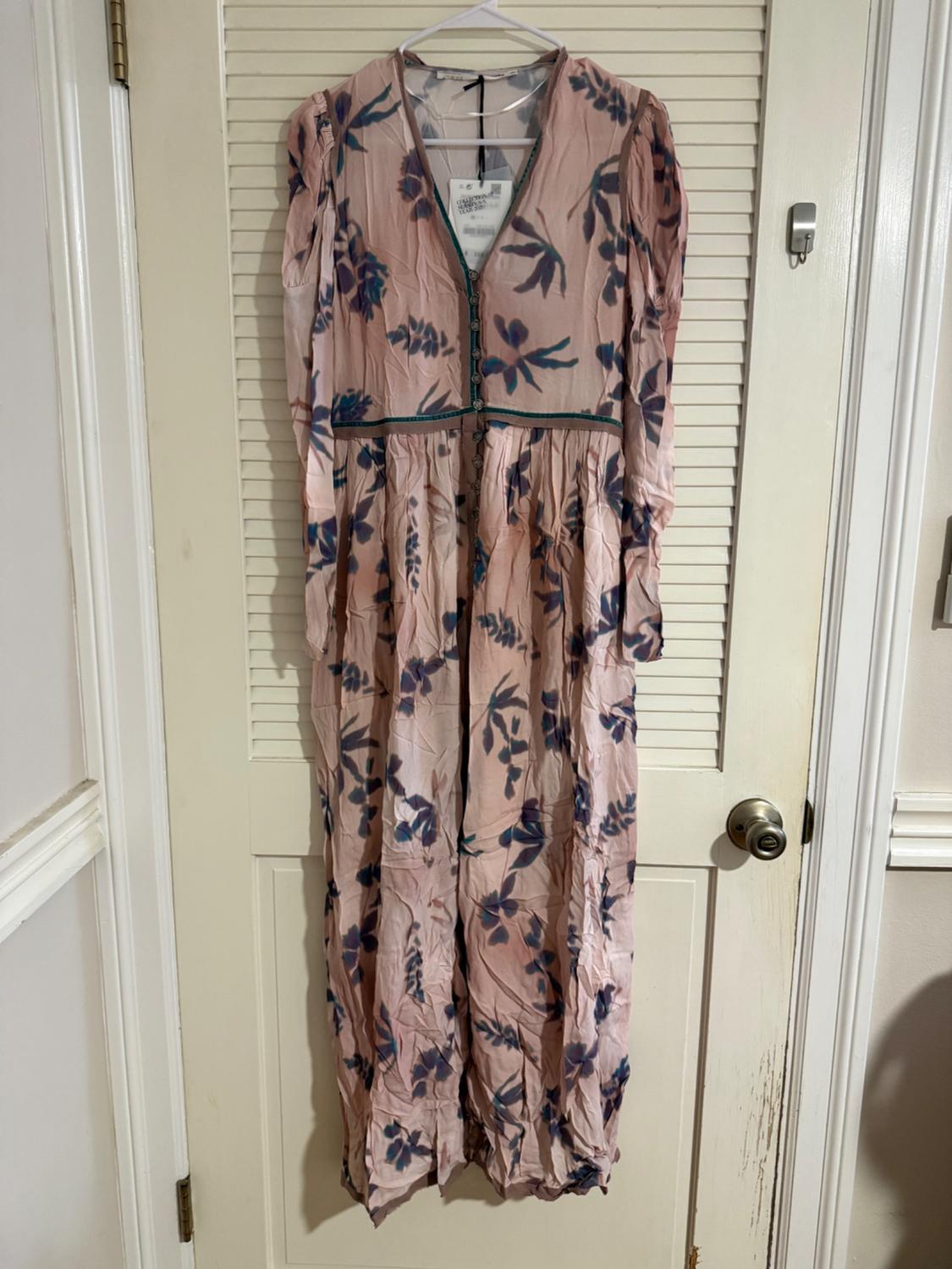 Long floral dress in pink and blue tones hanging on a white door. The fabric is wrinkled and has a front fastening.