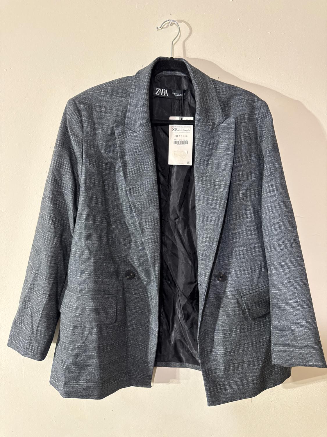 Gray blazer with a plaid pattern, hanging on a hanger. Visible tag with size XS and ZARA brand on the inside.