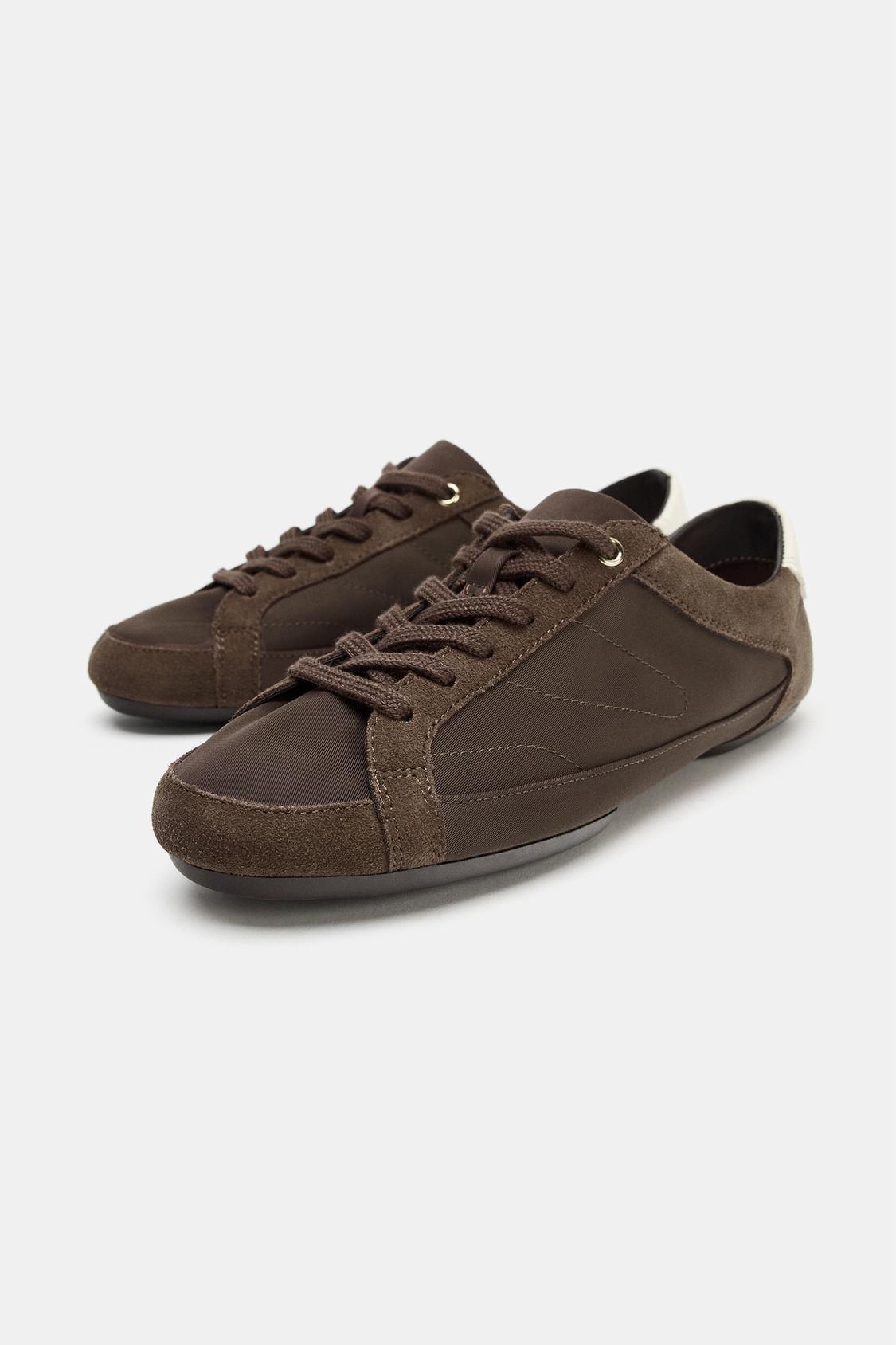 Zapatillas marrones de perfil bajo con cordones y detalles en el talón. Suela oscura y costuras visibles.