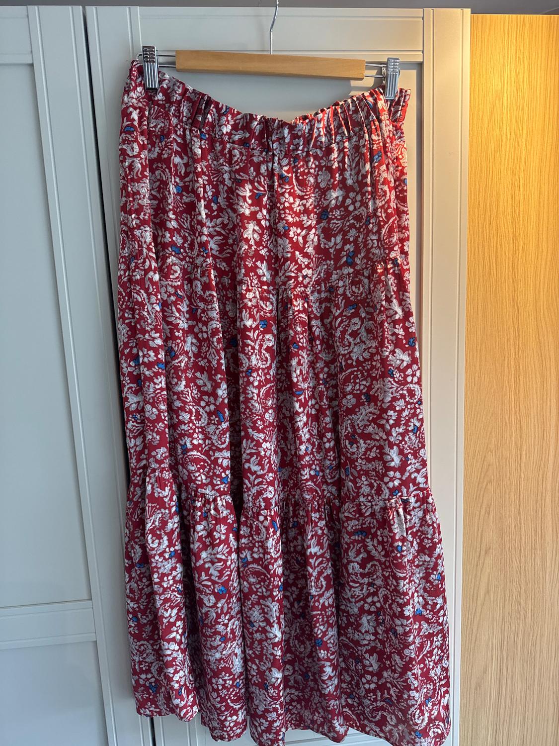 Red long skirt with white and blue floral print, hanging on a wooden hanger in front of a light wardrobe.