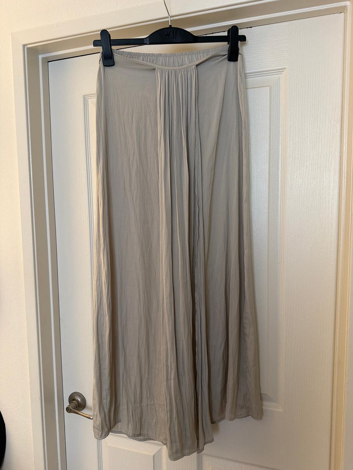 Long beige skirt hanging on a black H&M hanger over a white door. Lightweight, pleated fabric.
