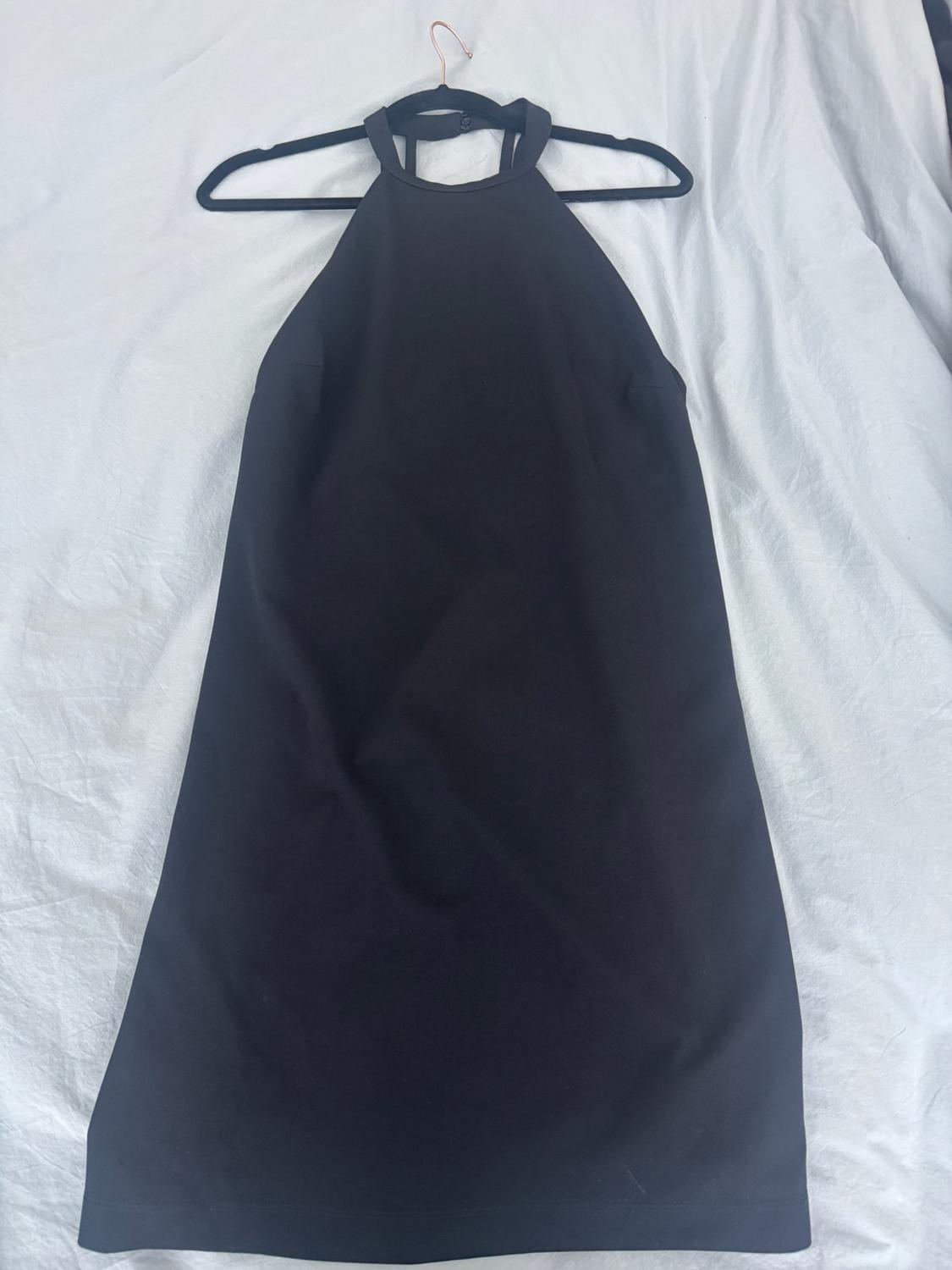 Short black halterneck dress hanging on a hanger over a crumpled white fabric.