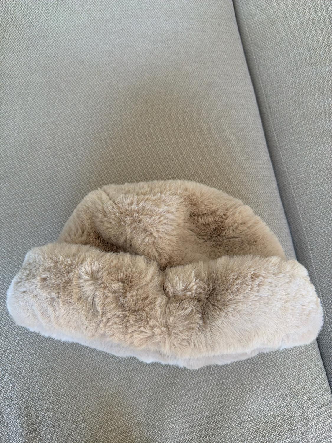 Light beige faux fur bucket hat resting on a textured grey fabric surface.