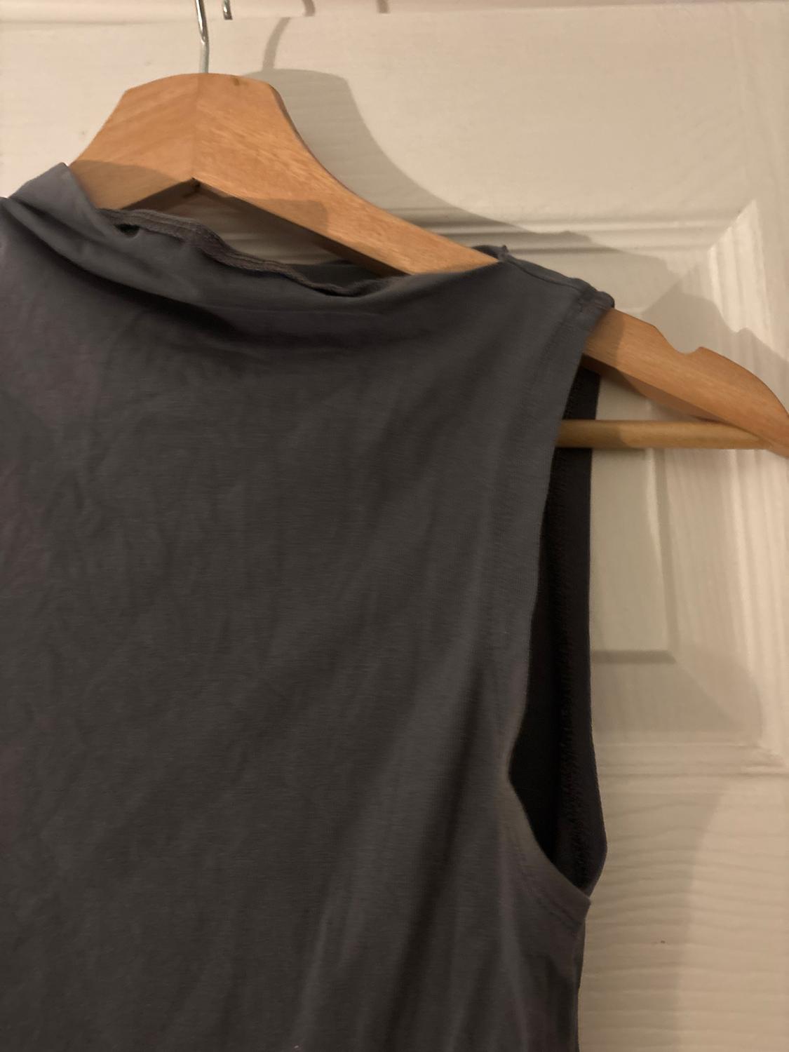 Grey sleeveless top hanging on a wooden hanger over a white door. The fabric appears soft and light.