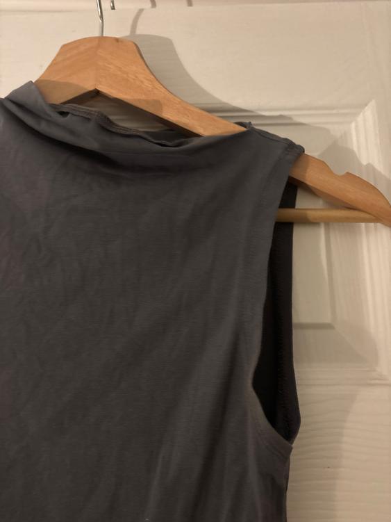 Grey sleeveless top hanging on a wooden hanger over a white door. The fabric appears soft and light.