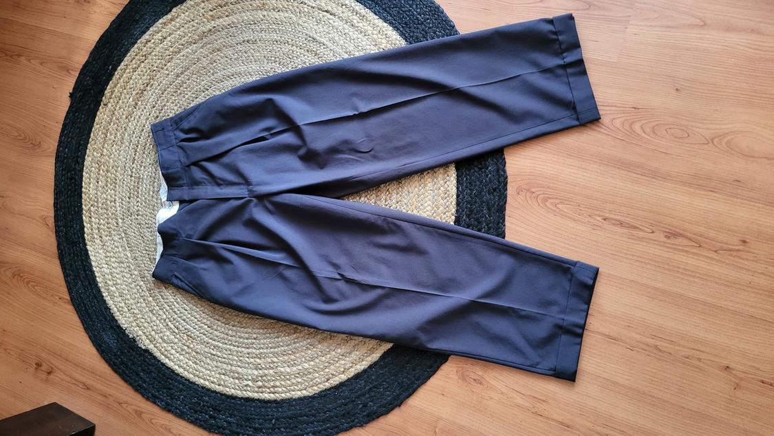 Grey soft fabric trousers placed on a round jute rug on a light wooden floor.