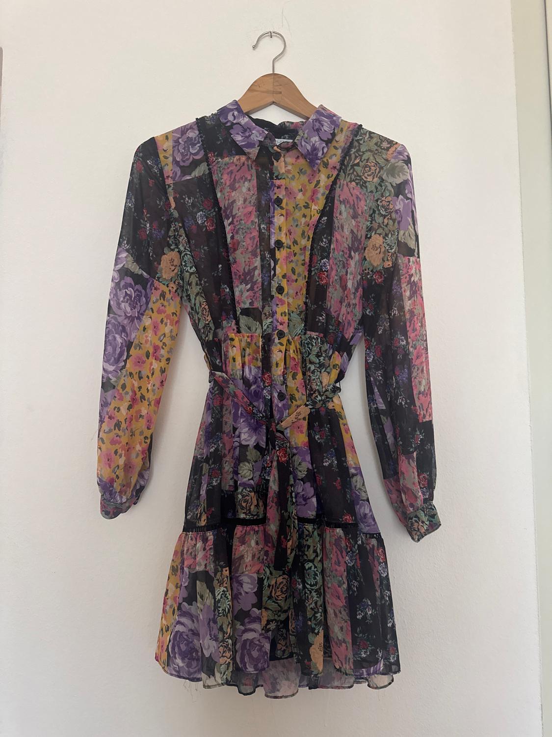 Multicoloured floral dress with long sleeves and a shirt collar, hanging on a wooden hanger against a white background.