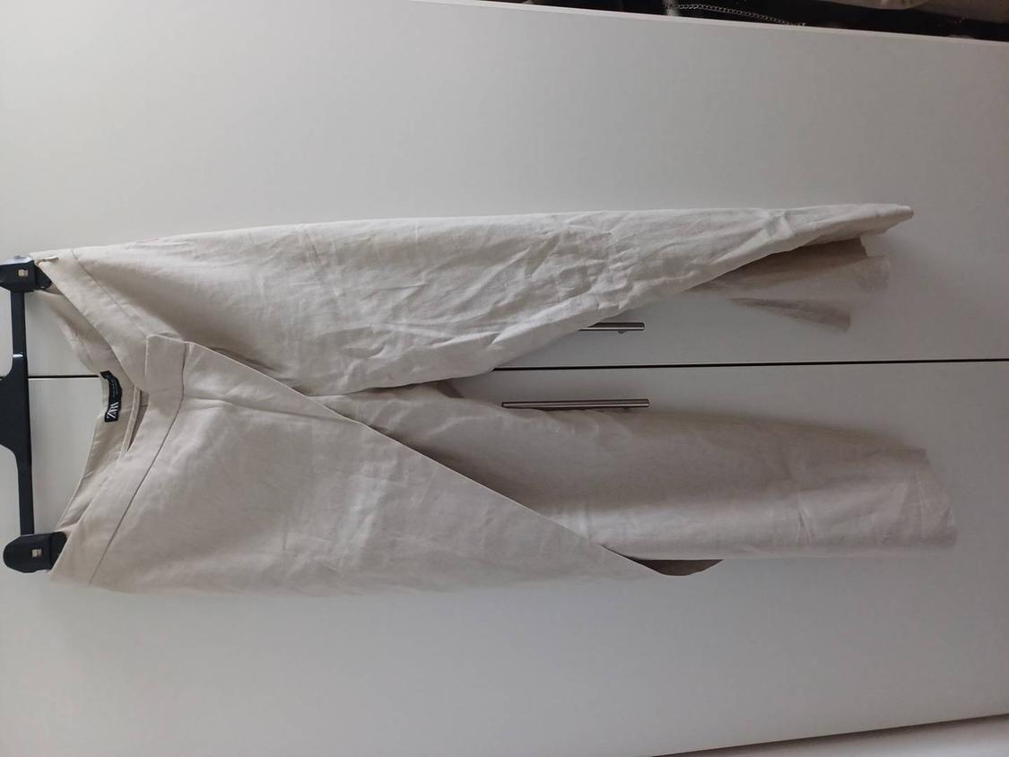 Beige trousers hung on a black hanger in front of a white wardrobe. Wrinkled fabric and simple design.
