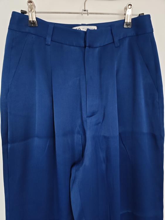Navy blue trousers hanging on a metal hanger with clips. Smooth fabric and visible pleats on the front.