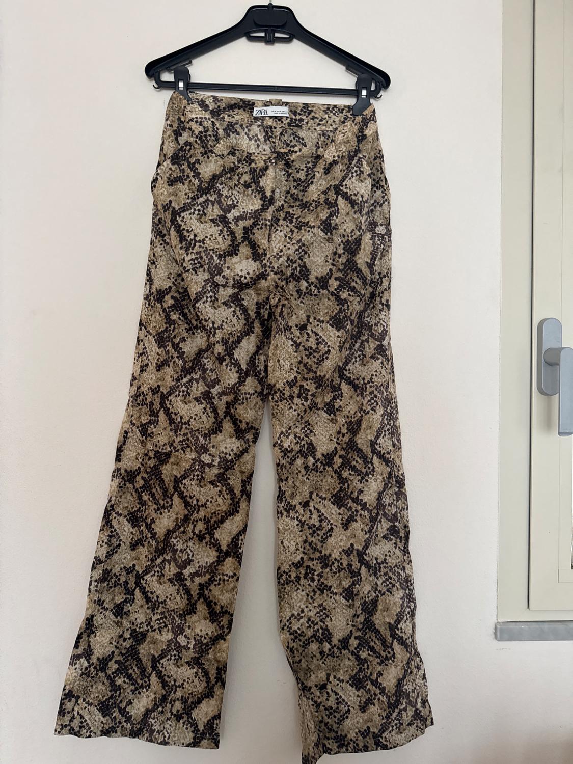 Snake print trousers in brown and black tones hanging on a black hanger. Visible label with the text "ZARA".