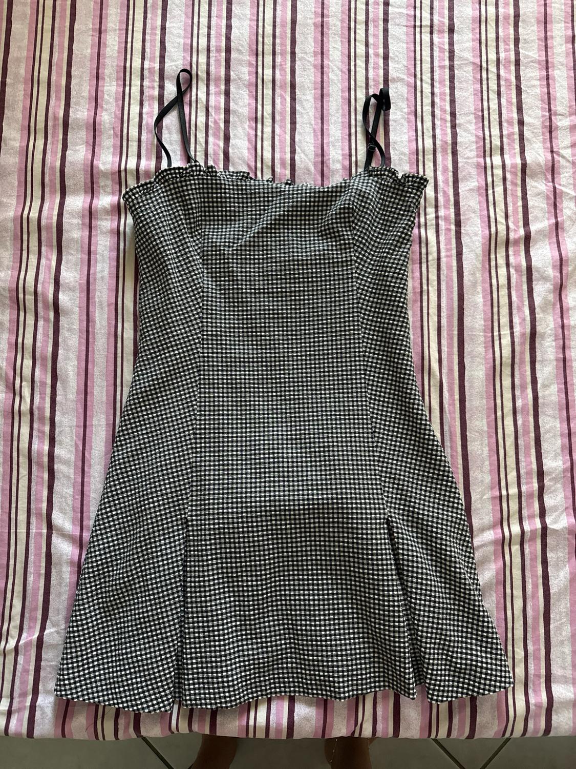 Short black and white checked dress with thin straps, laid out on a bed with pink and purple striped sheets.