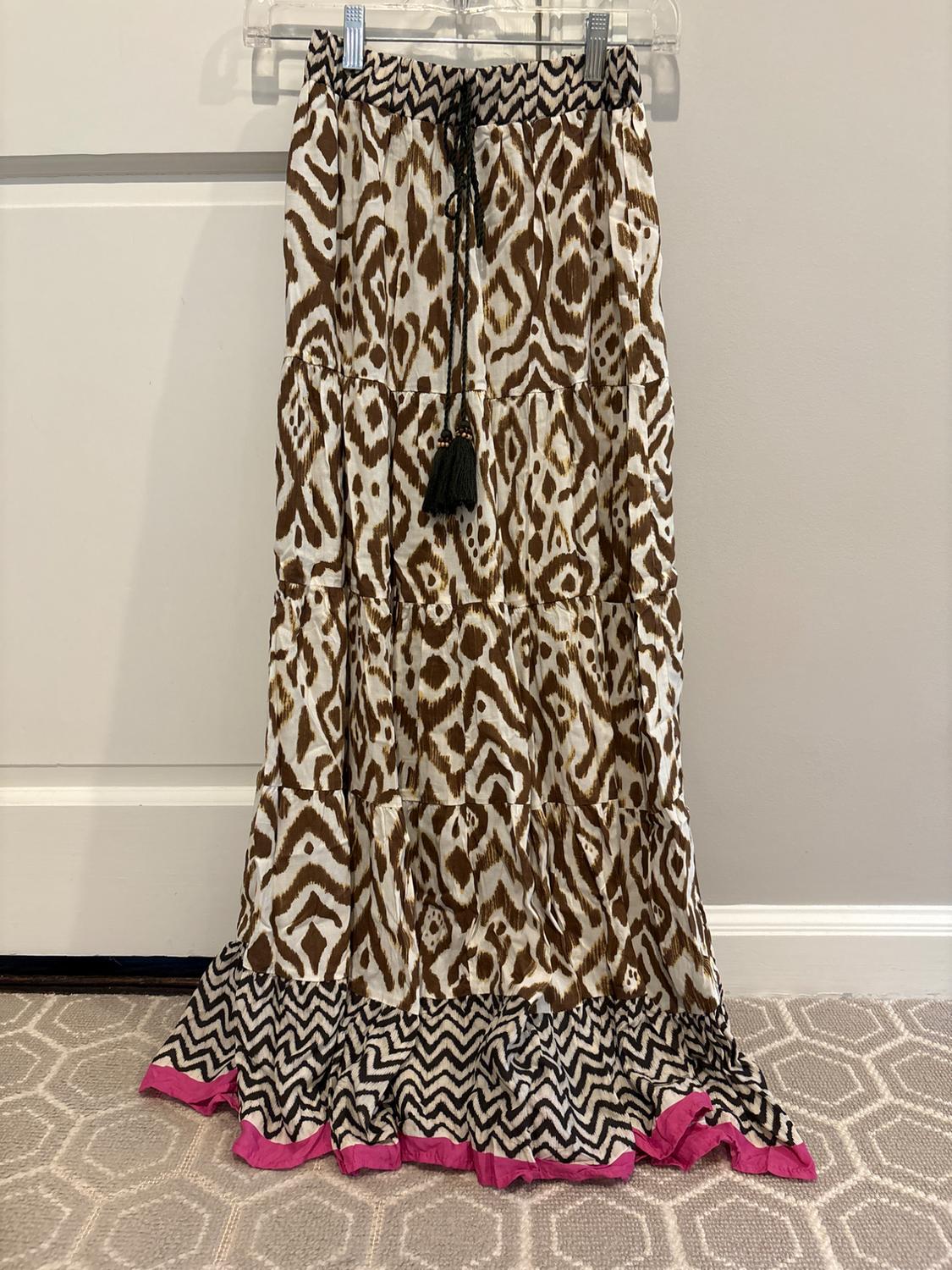 Long skirt with brown and white abstract print, black drawstring with tassels, zigzag hem and pink trim, hanging on a door.