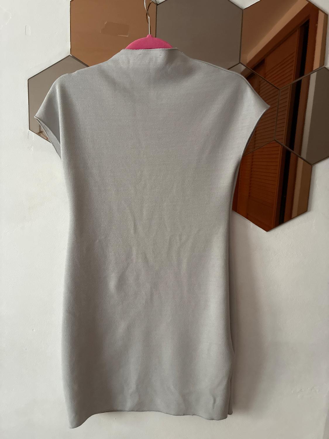 Light grey dress hanging on a pink hanger, reflected in a hexagonal mirror on the white wall.