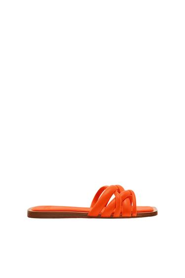 Orange flat sandal with interwoven straps. Side view on a white background with ample negative space above.
