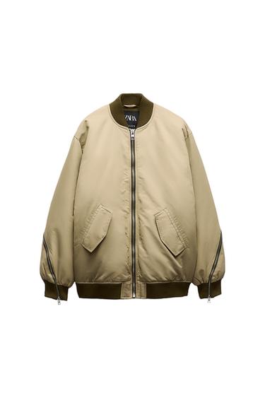 Front view of a beige jacket with a zip and side pockets. Elasticated collar, cuffs, and waistband in a dark colour.