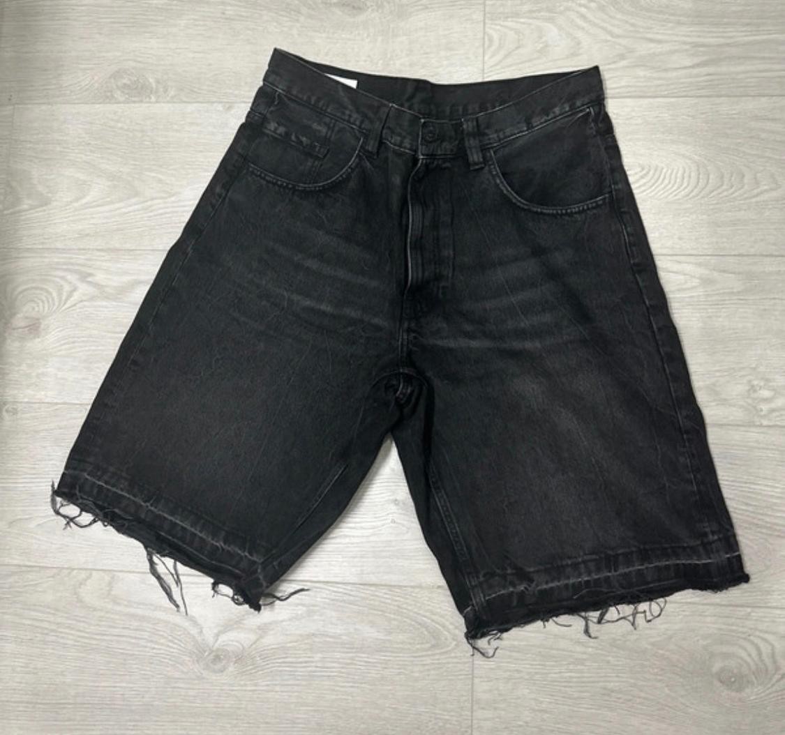 Black denim shorts with a washed effect and frayed hems, on a light wooden floor.