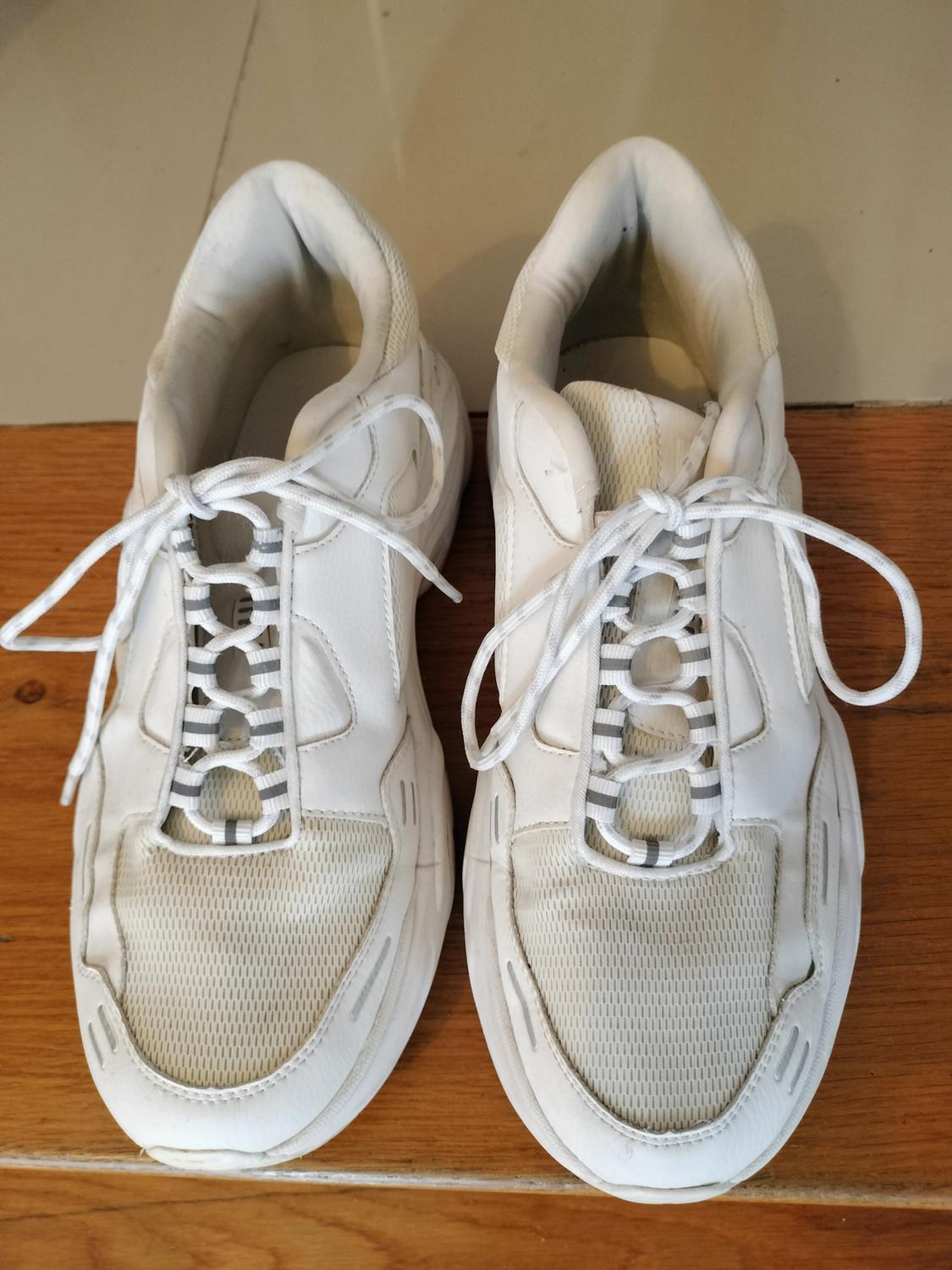 White trainers with chunky soles, striped laces and mesh details, on a wooden floor.