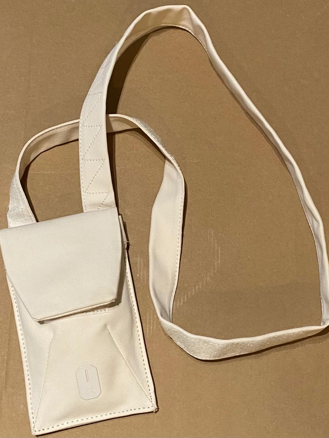 Small white handbag with flap and long strap on a brown background. Minimalist and modern design.